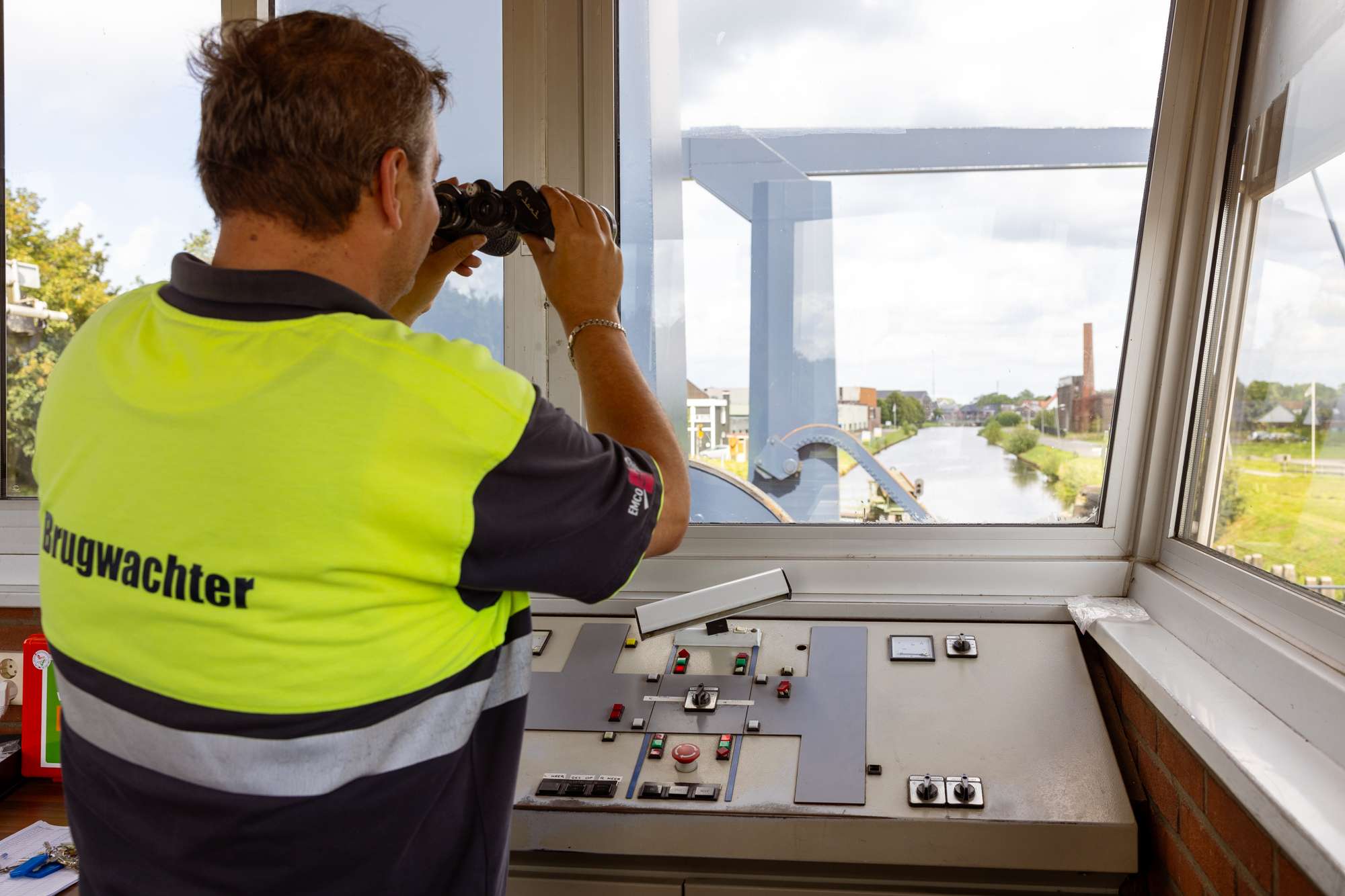 Brugwachter kijkt met verrekijker naar de verte