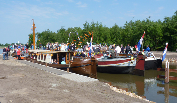 Foto van boten met mensen en vlaggetjes.
